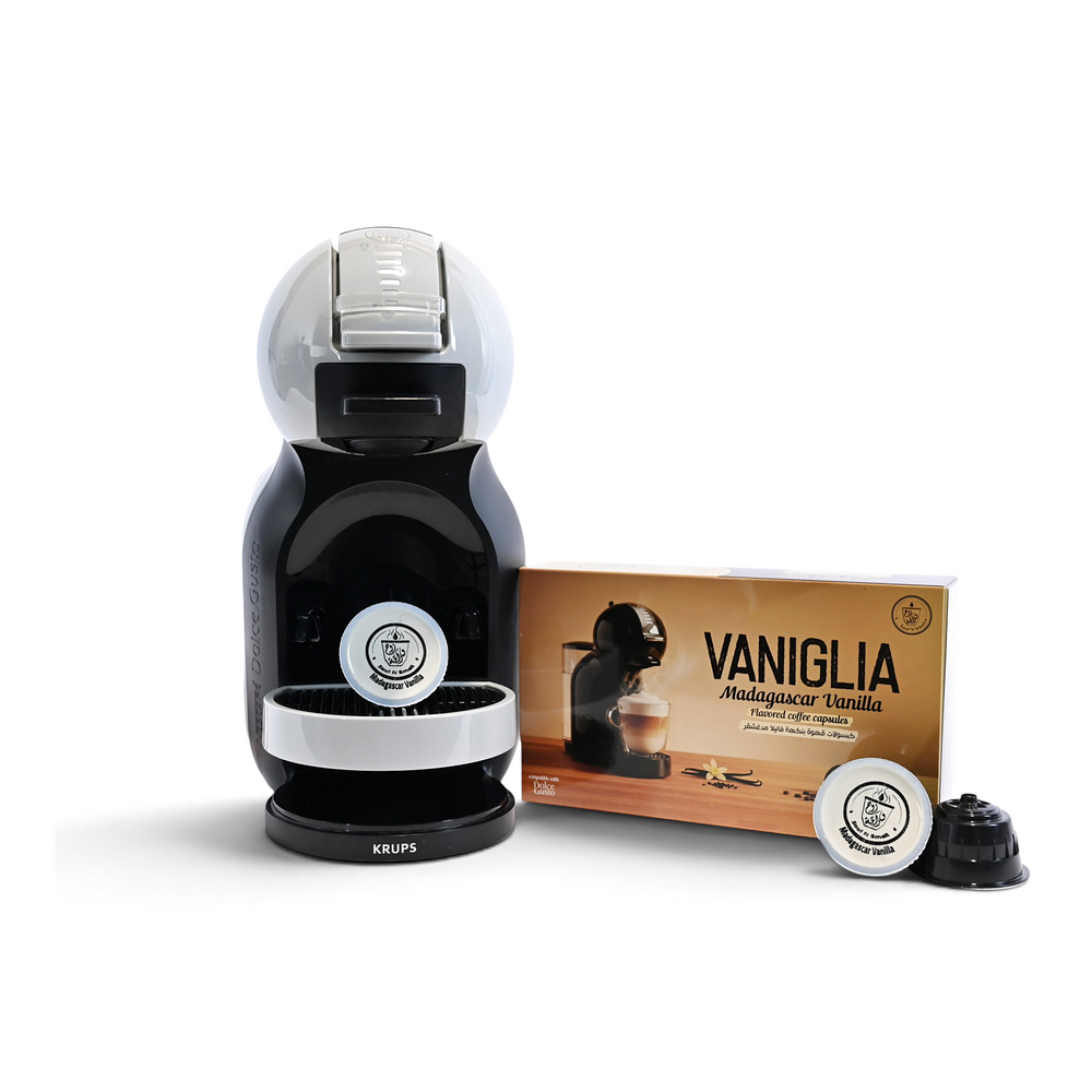 VANIGLIA - Vanilla Madagascar - A black and silver Krups Nespresso coffee machine shown next to a box of Vaniglia Madagascar vanilla coffee capsules and two capsules on a white background.