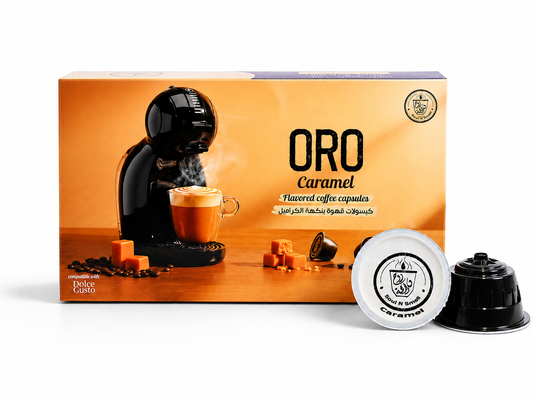 A box of Oro Caramel flavored coffee capsules with two capsules displayed in front on a clean white background. The packaging features a warm caramel-orange design with an illustration of a coffee machine making an espresso coffee.